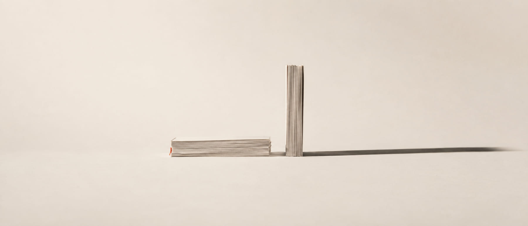 Una pila de hojas de papel sobre una mesa con la mitad superior retirada y apoyada de canto al lado, iluminada por una luz dura que proyecta una sombra larga.